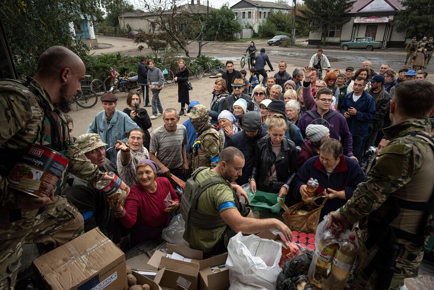 Ukrainian soldiers hand out food and drink from the back of a truck to residents lined up.