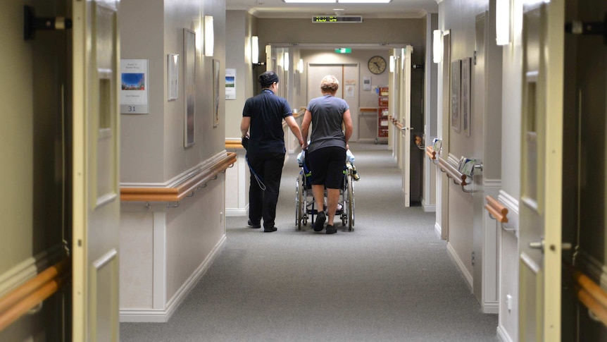 Nurses wheel a resident down a hallway in a nursing home.