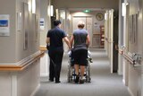Nurses wheel a resident down a hallway in a Brisbane nursing home