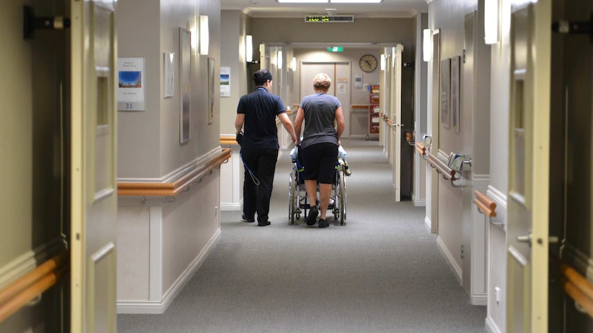 Nurses wheel a patient down a hallway in a Brisbane nursing home.