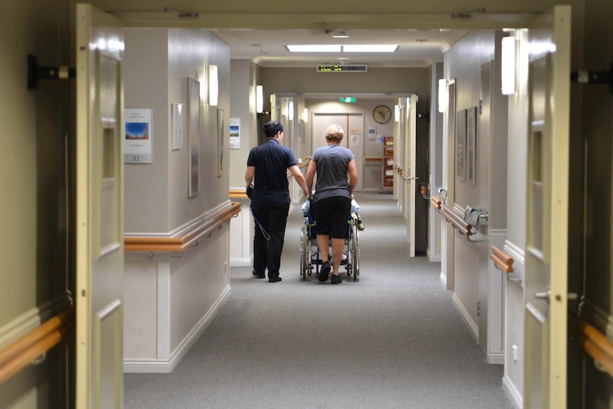 Nurses wheel a resident down a hallway in a nursing home.