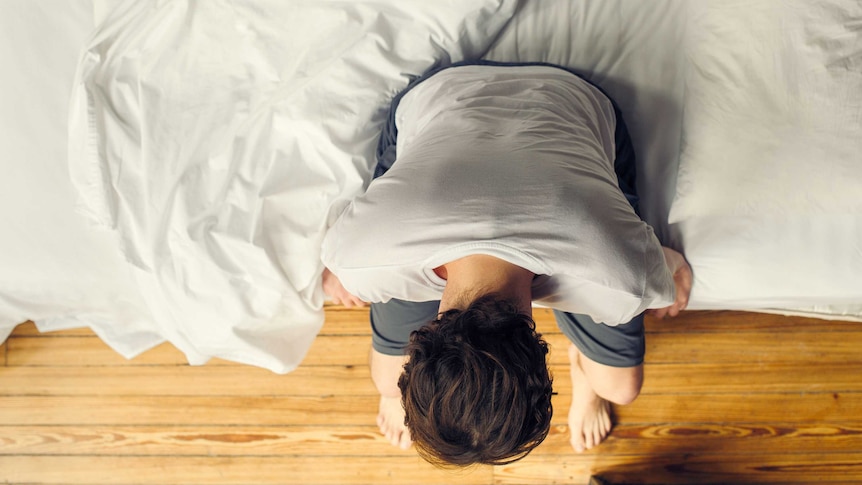 A man sitting on the edge of his bed.