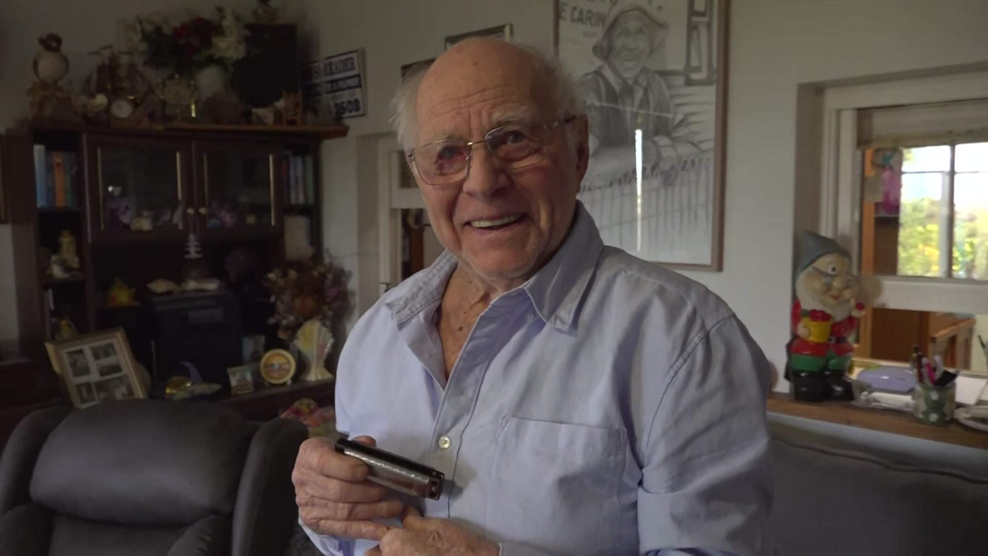 Elderly gentleman smiling while holding harmonica in lounge room.