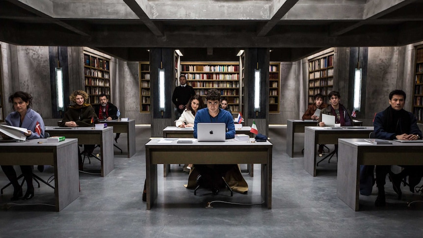 A scene from the movie The Translators with a group of people sitting at desks in a grey bunker