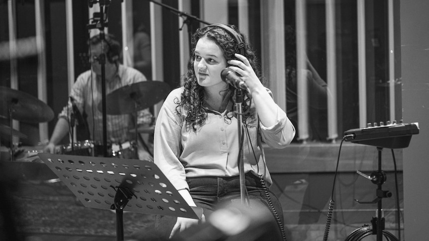 a black and white image of Minnie, a young woman with curly hair, sitting in studio with headphones on and a mic in front of her