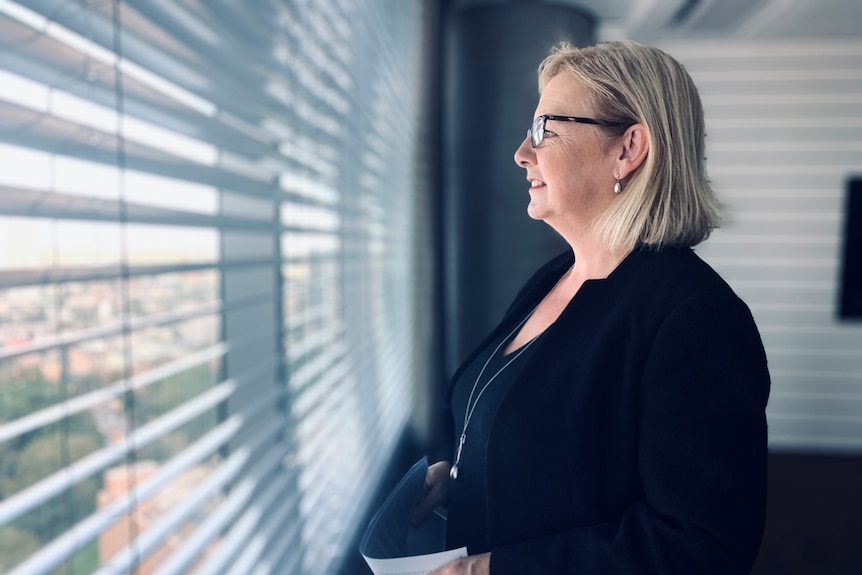 A woman in corporate clothing in an office staring out a window