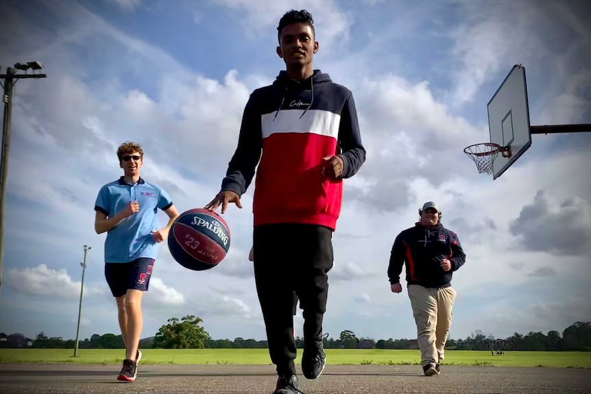 Three people playing basketball run towards the camera.