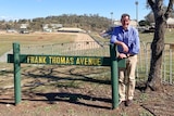 A man stands behind a sign that reads Frank Thomas Avenue