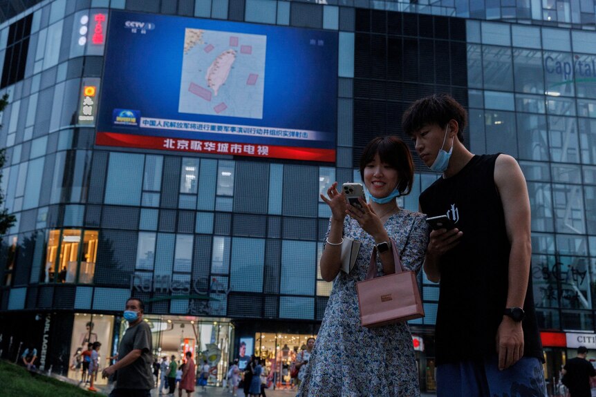 Two Chinese young people checking their phones in a square.