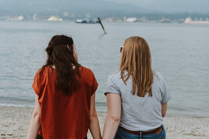 A teenaged girl and an older woman sit on a rock at the beach and look out to sea.