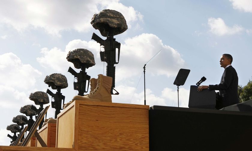 Barack Obama speaks at a memorial. Soldiers' boots, helmets and rifles are lined up in front of a stage.