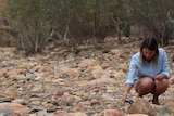 A woman kneeling to touch the ground in a rocky landscape