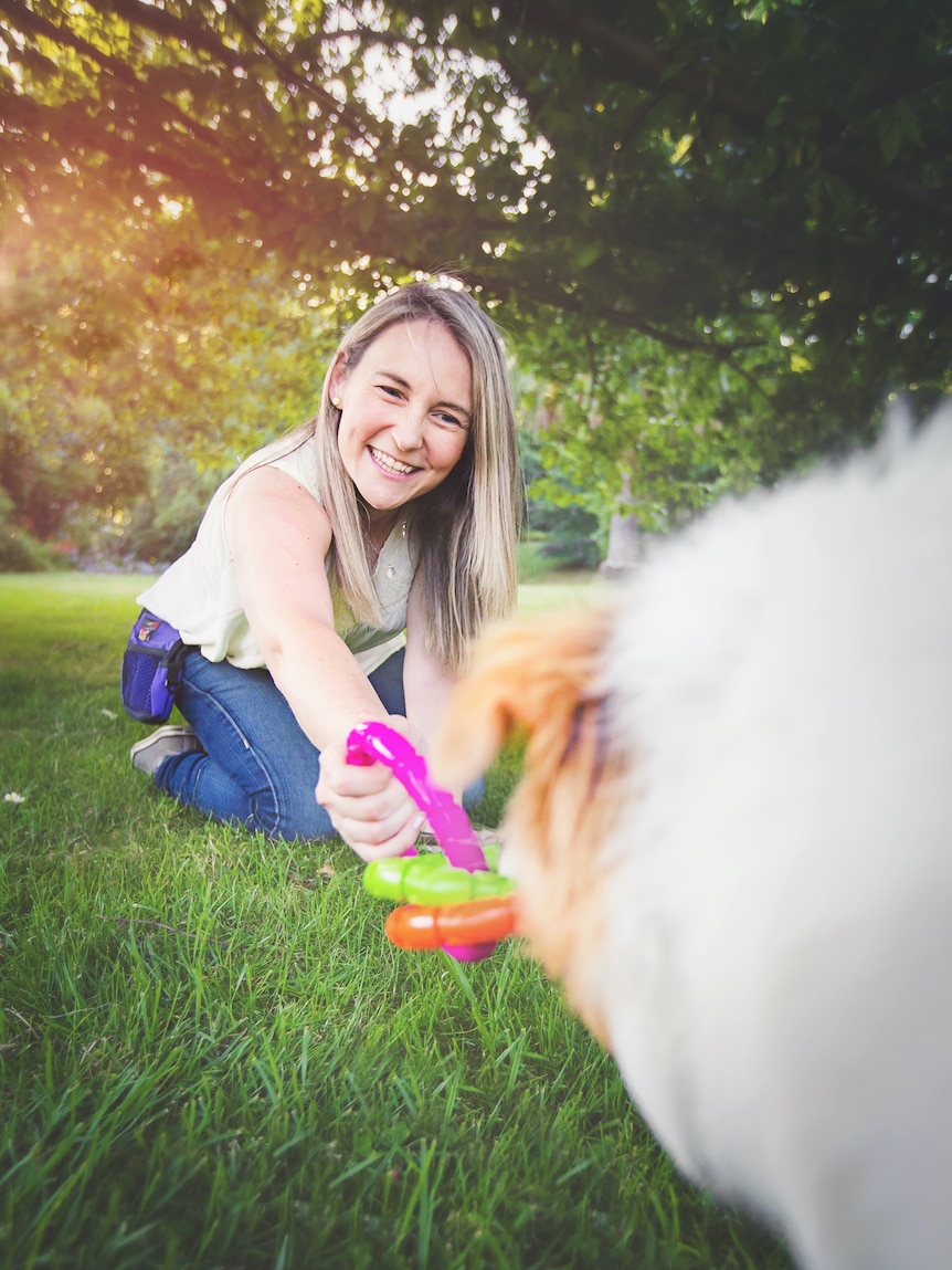 A woman smiles as she plays with a pet toy with a dog