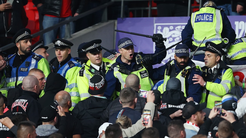 Police with batons raised at a group of men at a football match 