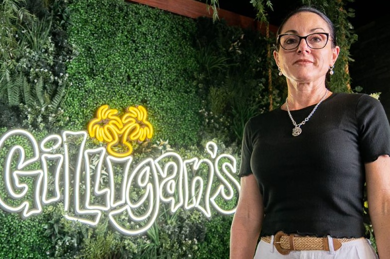 Woman in black t-shirt stands in front of a Gilligan's sign.