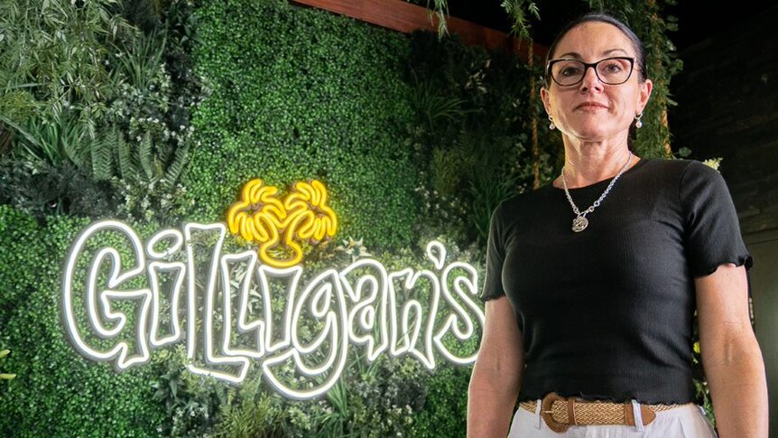 Woman in black t-shirt stands in front of a Gilligan's sign.