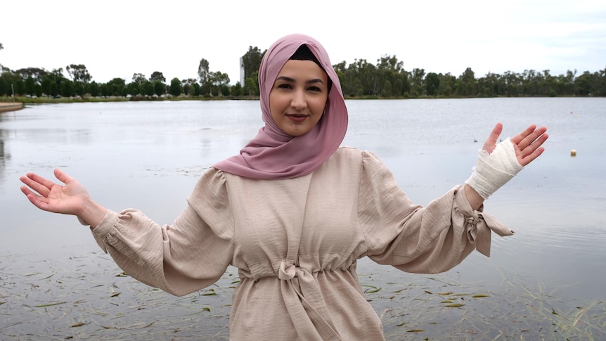 A woman standing in front of a lake with her arms raised high and her left hand bandaged
