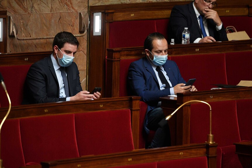French MPs sit in Parliament wearing face masks and looking at their phones