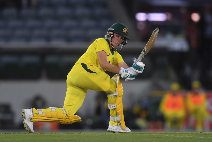 Beth Mooney paddles a ball down the leg side wearing the yellow Australian T20 uniform.