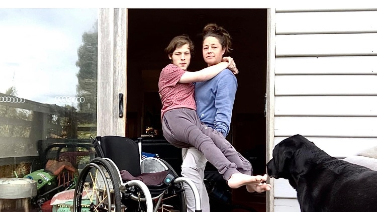 A woman lifts a young man out of his wheelchair