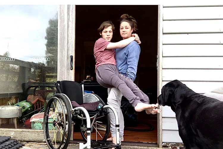 A woman lifts her son out of their wheelchair