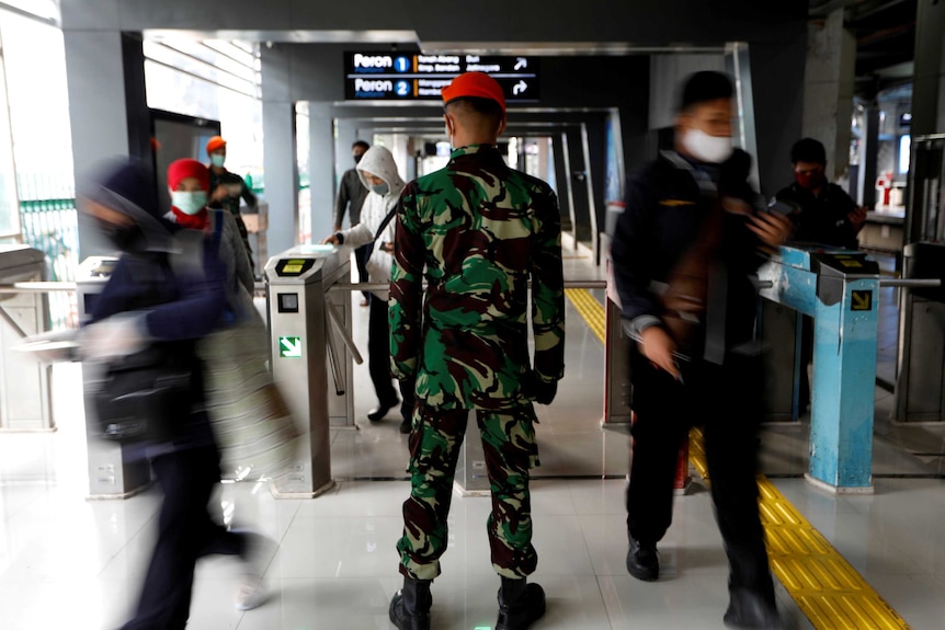 Commuters wear protective masks as Indonesian airforce personnel enforce social restrictions at Sudirman train station.