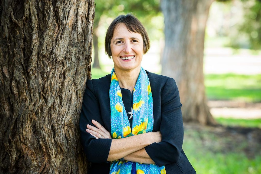 a woman smiling by a tree in a park