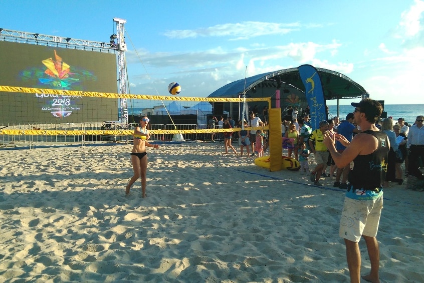 Two beach volleyball players playing, one each side of the net, while a crowd watches.