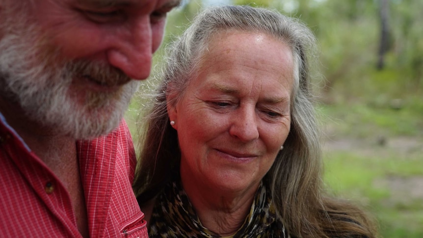 Sharon Cramp-Oliver, pictured with her husband Spud, look at a photo. They both look happy, and behind them is lush greenery.