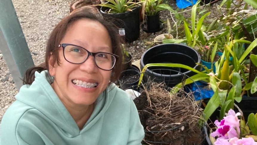 A woman with brown hair and glasses smiles while crouching next to pot plants