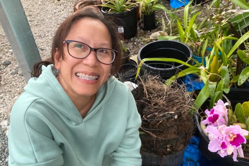 A woman with brown hair and glasses smiles while crouching next to pot plants