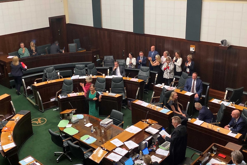 An above shot of Tasmania's House of Assembly members in Parliament. Some are clapping, others are talking with each other.