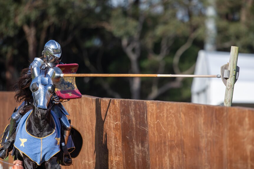 A knight in shining armour hits a small shield like target with a long lance
