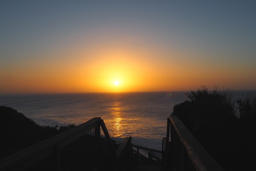 Timber stairs lead down to the ocean at sunrise.