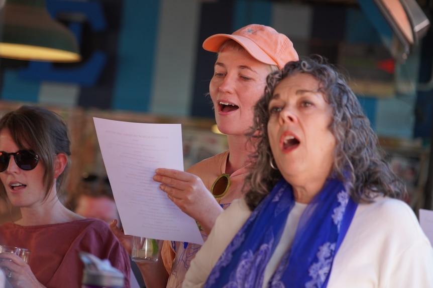 Two women stand side by side singing in a pub