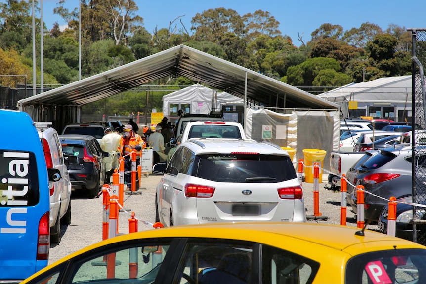 Rows of brightly coloured cars queue near a tent staffed by PPE-wearing testing workers in the sun.