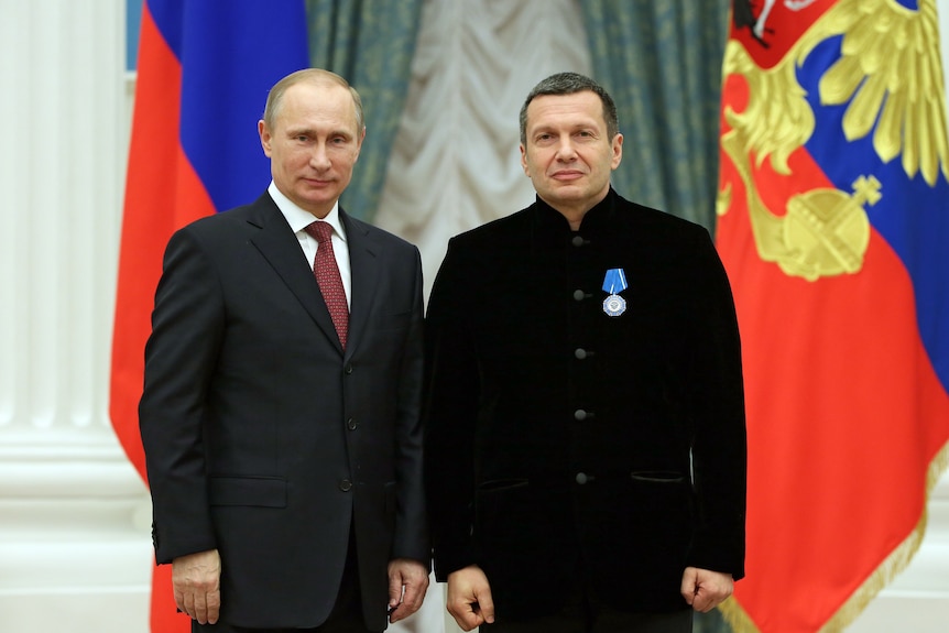 Putin stands next to a man wearing a medal.