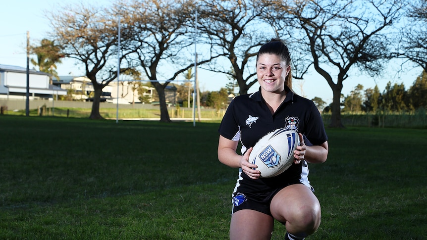 Kaarla Cowna kneels with a football with posts in the background.