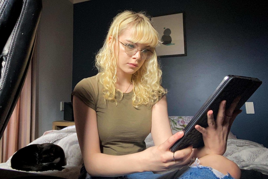 Lila Ritchie sits on the bed reading a tablet