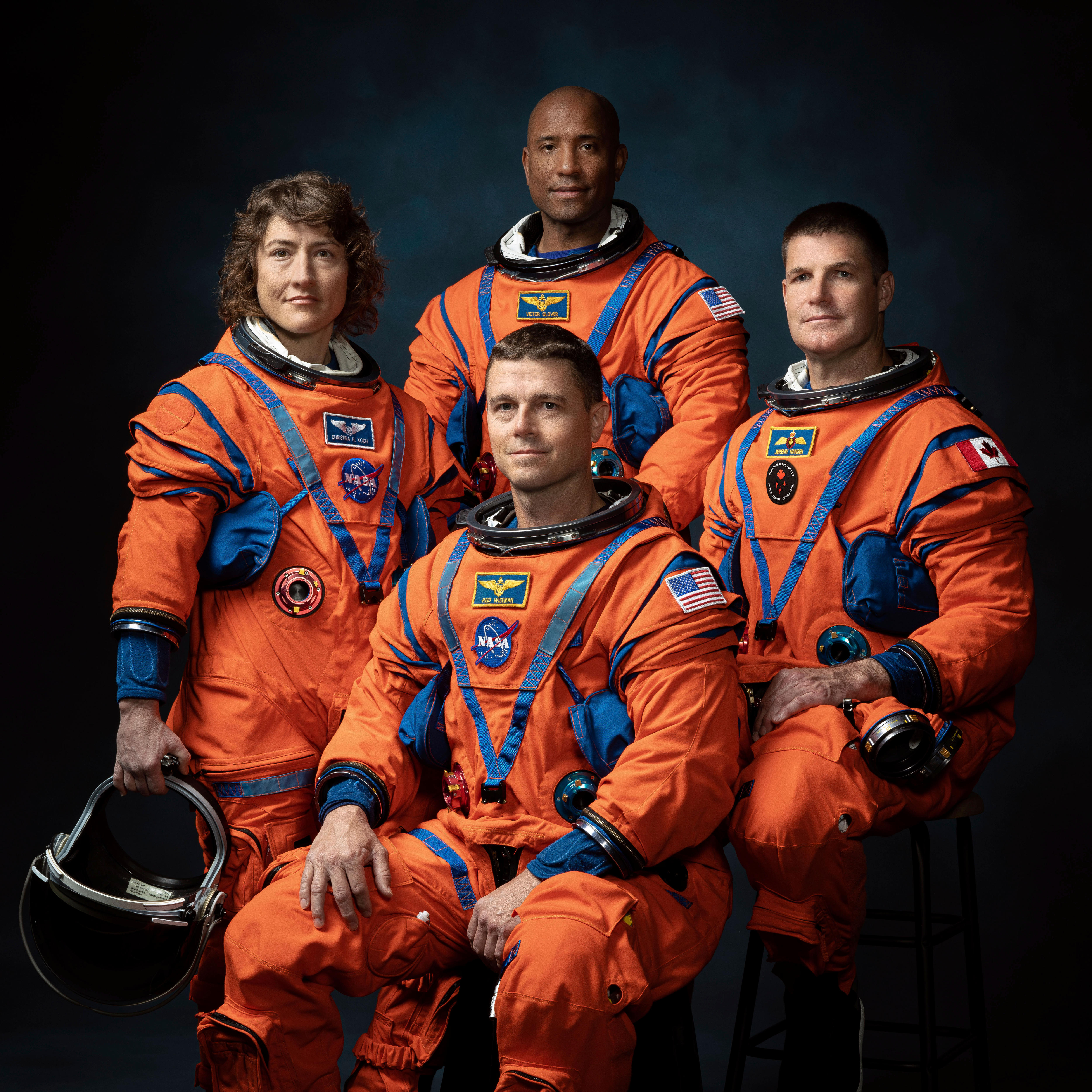 The four astronauts pose for a photo wearing orange suits. 