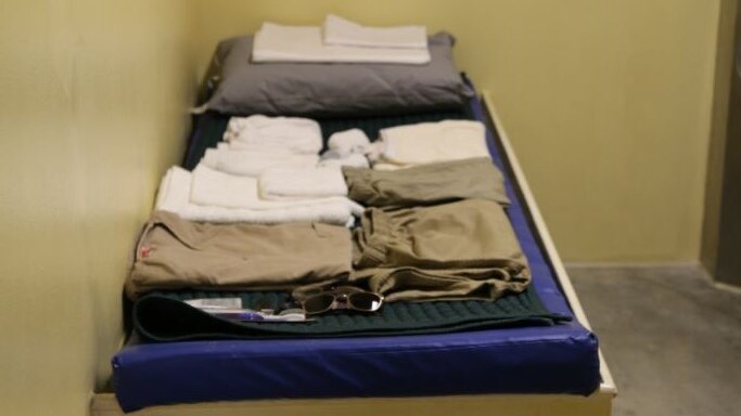 Clothes, sunglasses and toiletries are laid out on a bed in a cell.