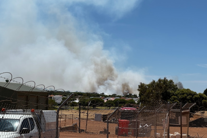 Smoke rises from a bushfire burning near buildings.