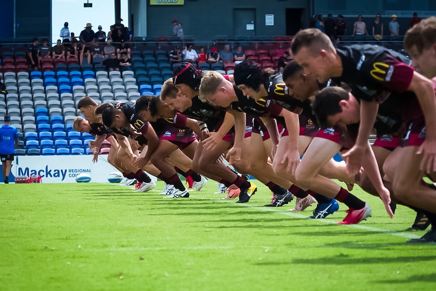 Row of teenagers in football shirts train in stadium.