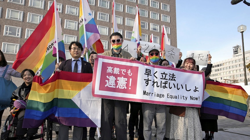 A group of LGBT supporters holding banners and flags gather outside a court in Japan.