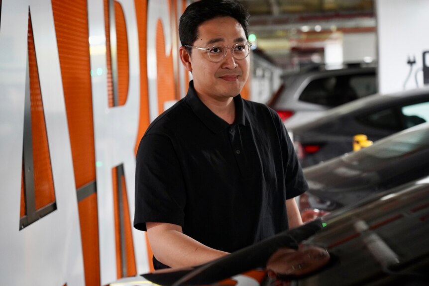 A man with glasses standing next to a black car in an underground carpark