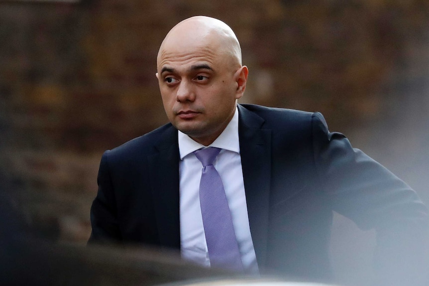 Sajid Javid wears a suit while he appears to be walk towards a car