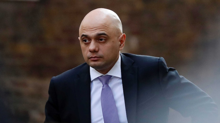 Sajid Javid wears a suit while he appears to be walk towards a car