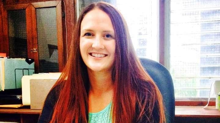 Photo shows a woman smiling at a desk.