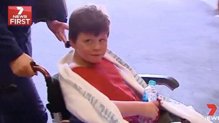 A boy holding a bottle of water sits in a wheelchair.