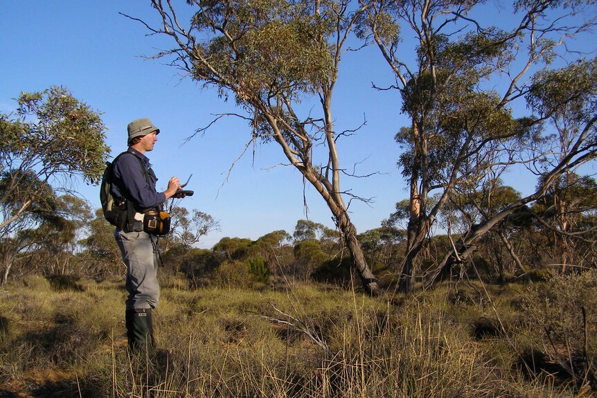 A man stands in the Australian outback holding equipment